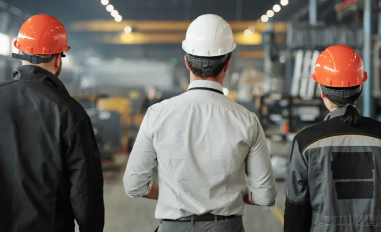 Three men wearing hard hats stand at a plant, ready to get manufacturing sales training & course.