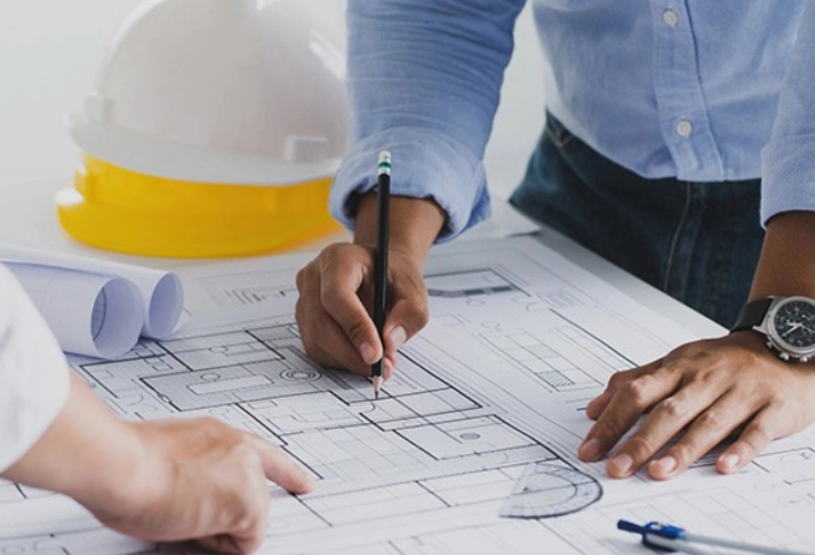 Two people working together on blueprints at a construction site for planing while wearing hardhats 