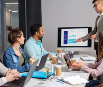 A man speaks in front of a group of people in a meeting room for import-export-sales training.