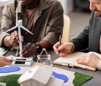 Three men work together on the windmill project, examining blueprints and plans, and taking notes.